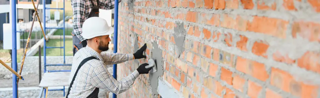 Handwerker trägt frischen Putz auf eine alte Backsteinwand auf – Vorbereitung zum Fassade sanieren.