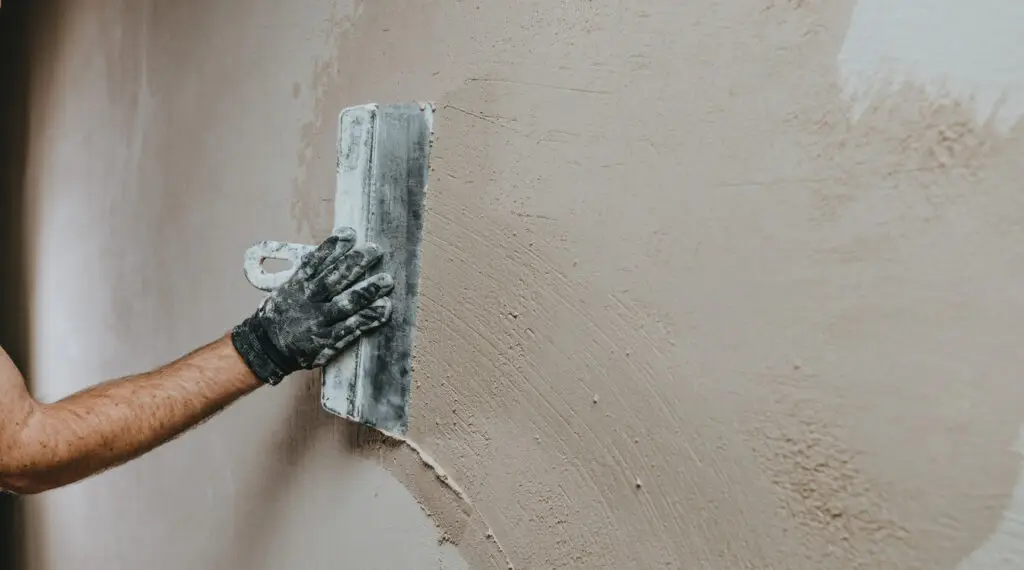 Handwerker in Arbeitskleidung verputzt eine Wand mit einer Kelle – horizontales Bannerbild mit Platz für Text, aufgenommen auf einer Baustelle in Bonn. Ausgeführt von Stuck Becker.
